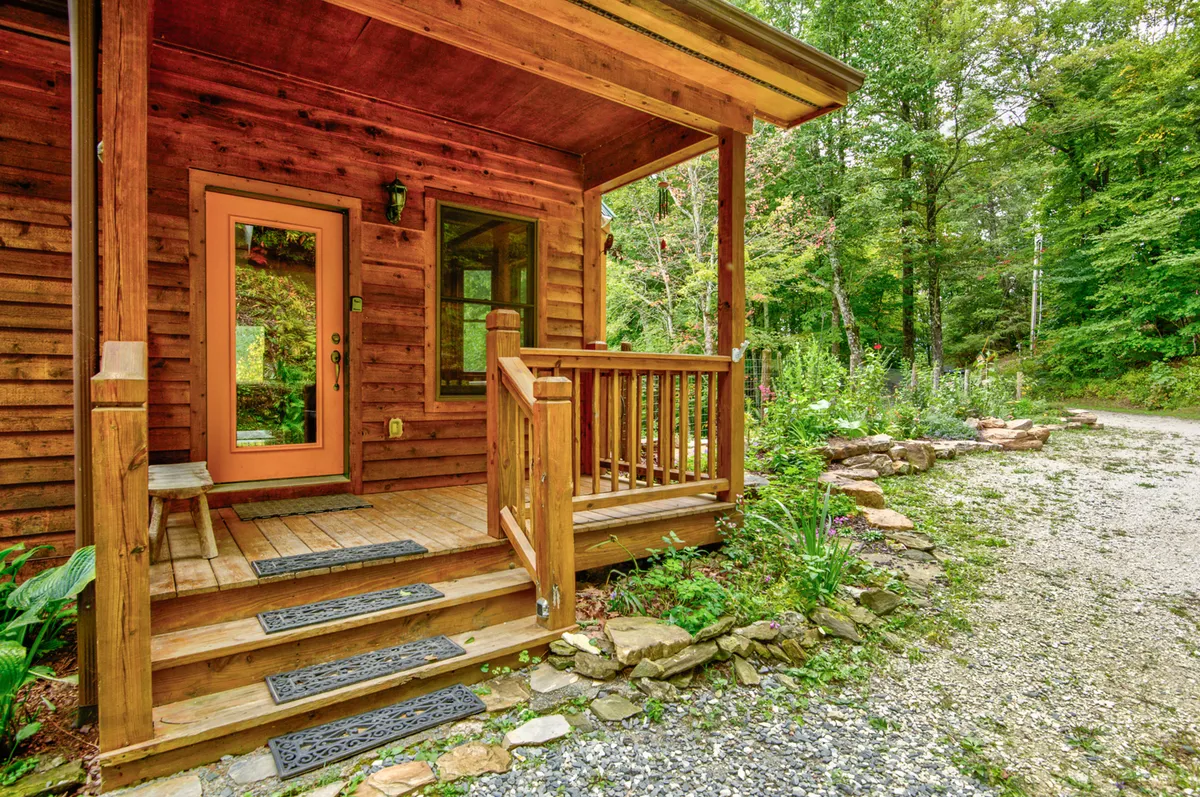 A welcoming wooden porch frames the front door amid vibrant greenery. The scene suggests the arrival experience and connection with the outdoors, echoing the journey and sense of welcome for guests venturing into the mountains with their EVs.