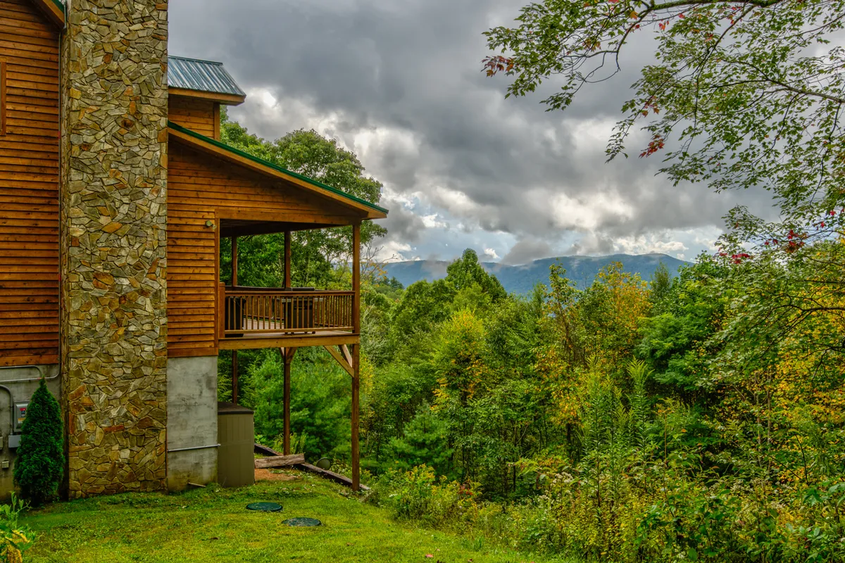 This image features a wooden structure with a stone chimney and balcony, set against a mountain view and surrounded by trees. The setting highlights the remote, natural environment and the kind of mountain retreat EV travelers might seek. Visible outdoor features and the mountain backdrop emphasize both seclusion and scenic beauty.