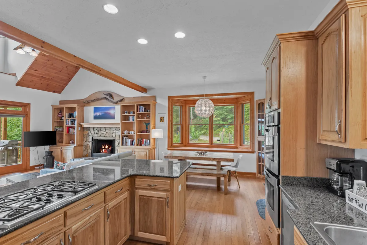 A welcoming open-plan space featuring a kitchen island, adjacent dining area, fireplace, and large windows. The kitchen area is visible with modern appliances and cabinetry, while the dining area and living space are seamlessly connected—perfect for family meals or board game nights.