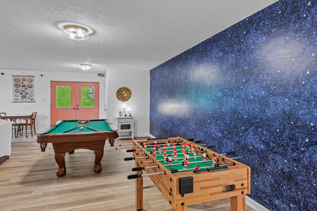 A lively game room featuring a pool table, foosball table, a colorful wall mural, and pink accent doors. The space is designed for fun, socializing, and relaxation with friends or family members.