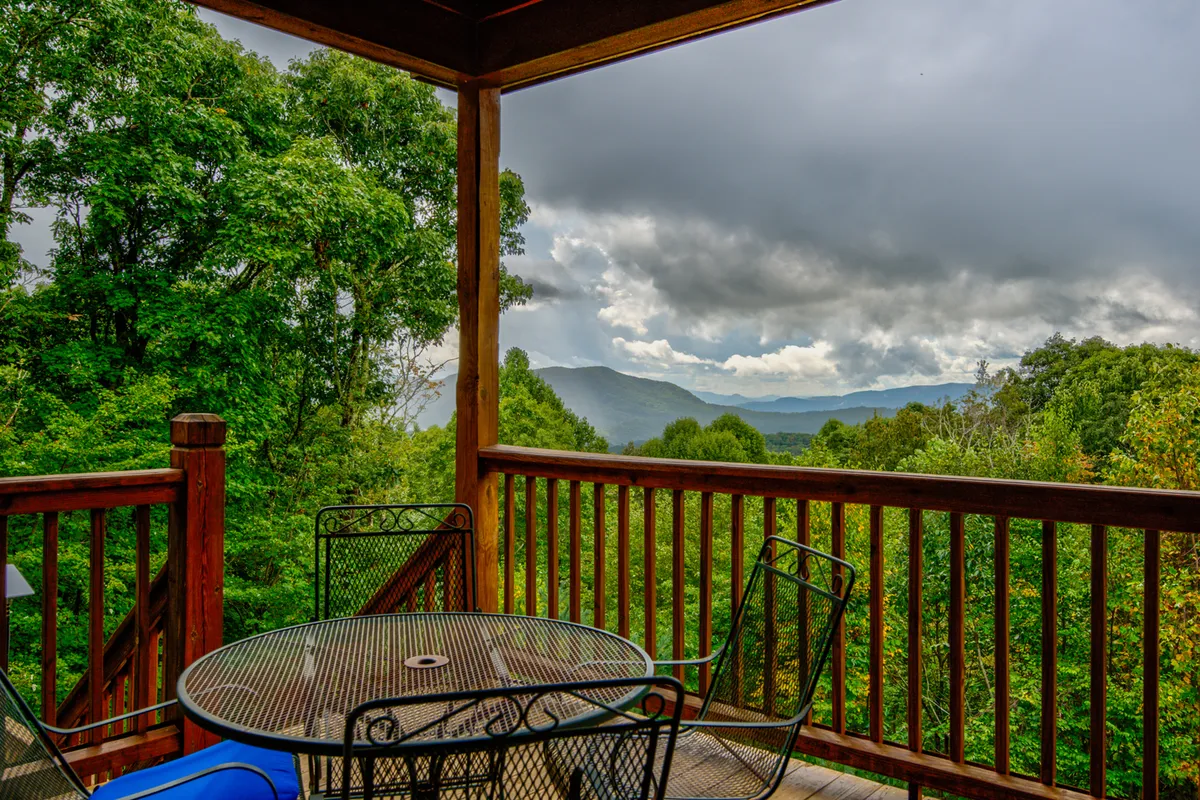 A tranquil outdoor dining area on a deck, offering sweeping mountain views through the railing. The table is set for enjoying meals al fresco, with a serene backdrop ideal for relaxation or stargazing.