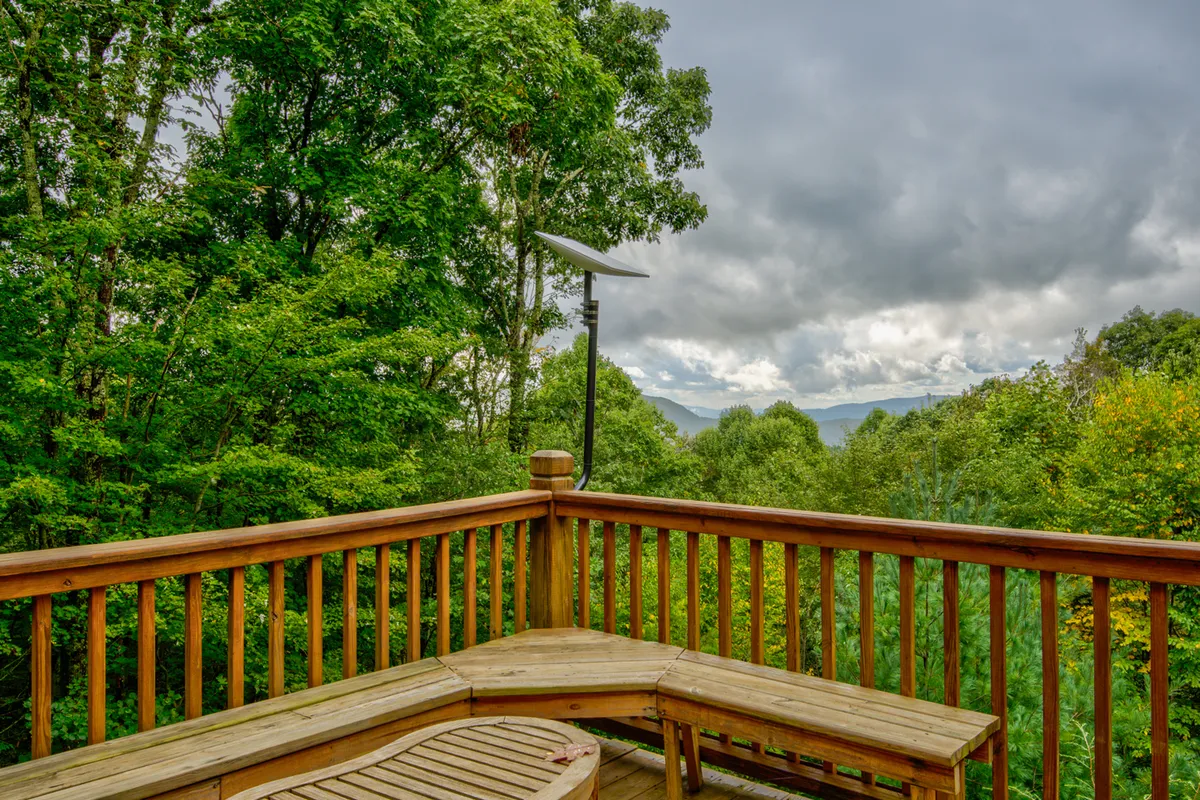 A spacious wooden deck overlooks lush greenery and distant mountains under a cloudy sky. The deck offers space for relaxation and social gatherings while connecting guests with natural views—key for those recharging both car and spirit overnight in a peaceful setting.