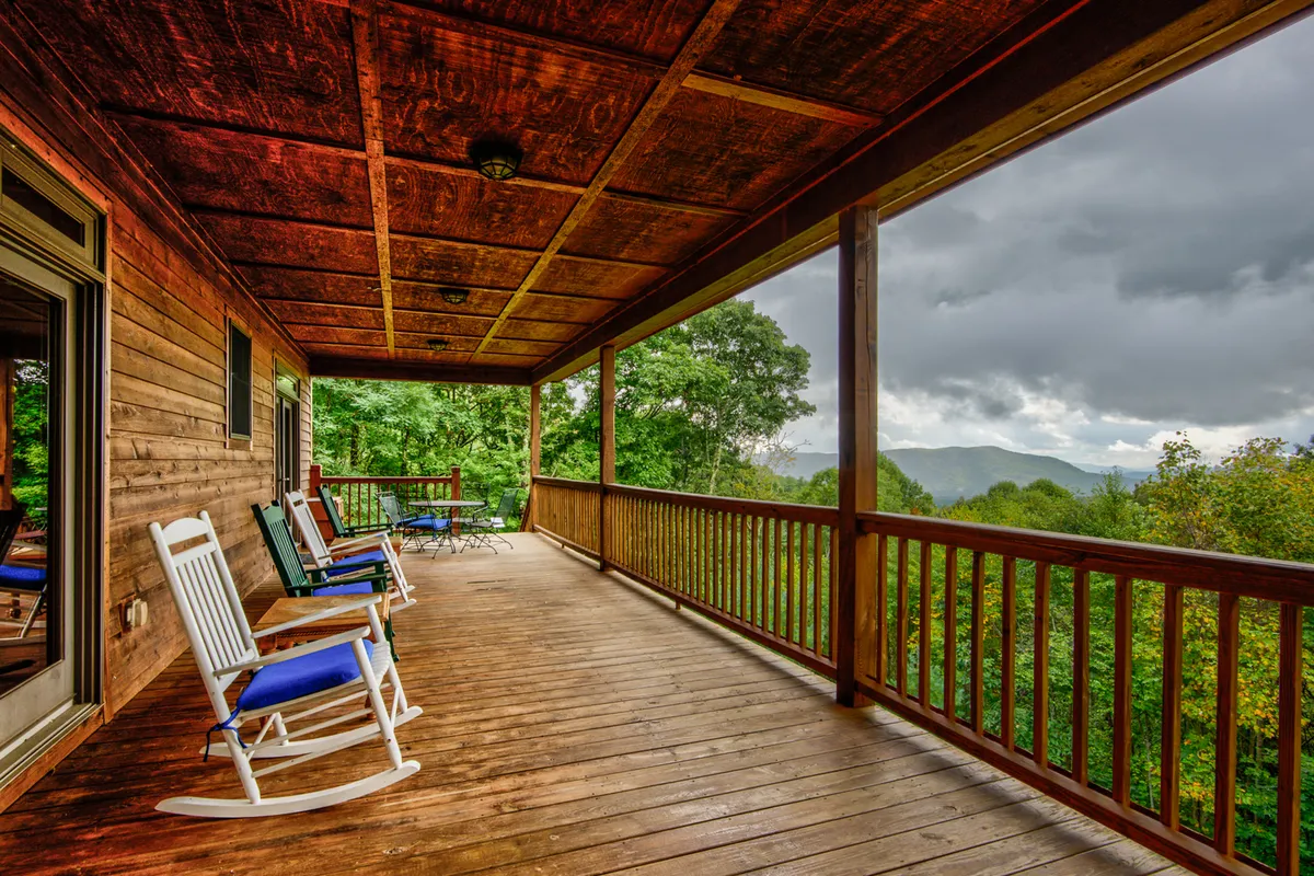 The covered deck features wooden rocking chairs and a table, all facing an expansive mountain view. The atmosphere is peaceful and inviting, ideal for relaxing after a day outdoors.