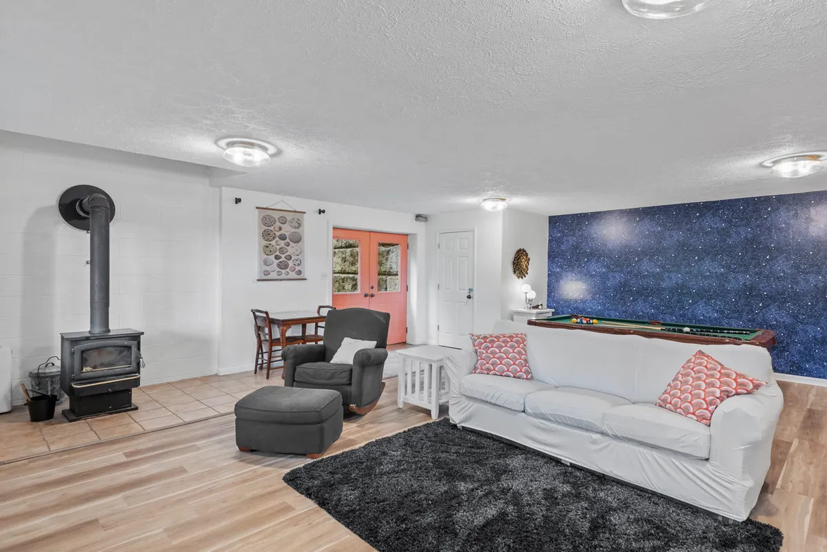 The image highlights a cozy corner of the game room, featuring a pool table, wood-burning stove, a textured wall with starry designs, and a brightly colored door. The room exudes a playful yet intimate atmosphere, perfect for game nights or relaxing by the fire. The design details add a touch of whimsy and warmth to the environment.